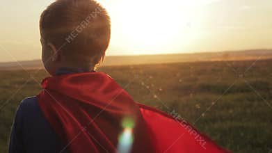 Boy superhero in a field at sunset