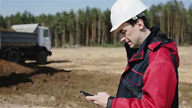 The builder in white helmet is typing number on the mobile phone and making call.