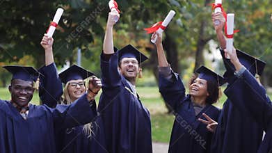 Happy students in mortar boards with diplomas