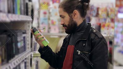 Men with beard and long hair selecting antiperspirant in supermarket.