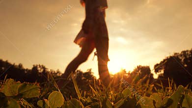 Slim blurred barefoot girl crossing the frame holding her high heel shoes in her hand, 4K clip. Orange sunset colors