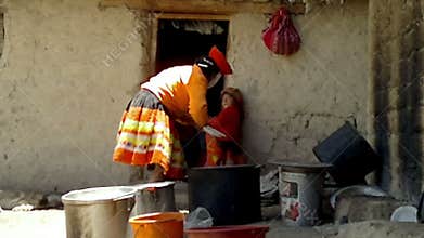 Peruvian woman dressed in colourful traditional handmade outfit and washing a plate in front of her house, Pata