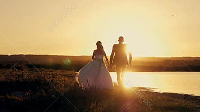 Bride and groom running through the field to meet the sun at sunset