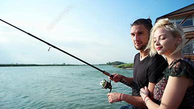 Happy couple fishing on spinning together at sunbeam, lovely couple sitting with rod on quay