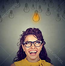Woman in glasses looking up at idea light bulb above head