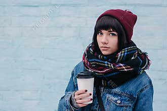 Young beautiful brunette girl drinking coffee on a cold street