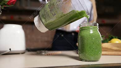 Pouring fresh green smoothie from blender into jar