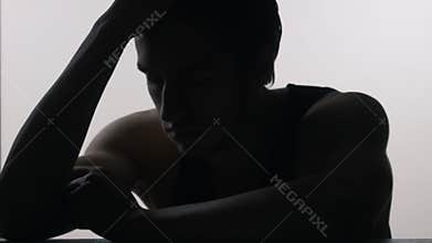 Silhouette of depressed, sad young man sitting at the table