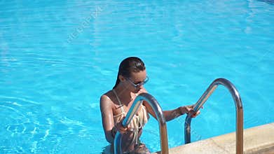 lady in swimsuit and sunglasses gets out the pool