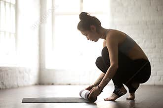 Young attractive woman unrolling yoga mat, white loft studio bac
