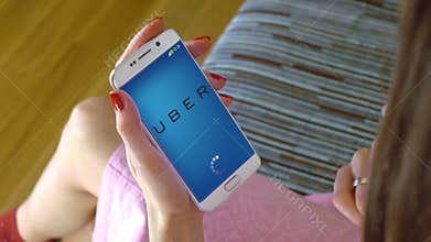 Young woman holding a cell phone with loading Uber mobile app. Conceptual editorial 4K clip