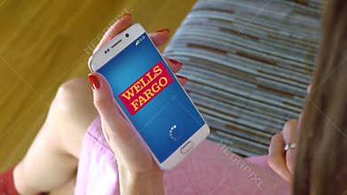 Young woman holding a cell phone with loading Wells Fargo mobile app. Conceptual editorial 4K clip