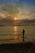Fisherman using net to catch fish during sunset
