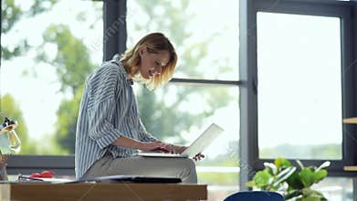 Joyful female student sitting on table while studying online