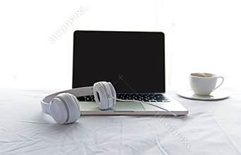 Morning music background. Coffee with laptop in white bed, sheet, duvet and pillow, messed up.