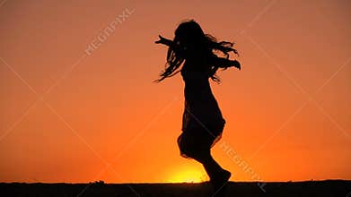Silhouette of young girl dancing at sunset