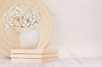 Soft home decor of beige bamboo dish and white small flowers in ceramic vase on white wood background. Interior.