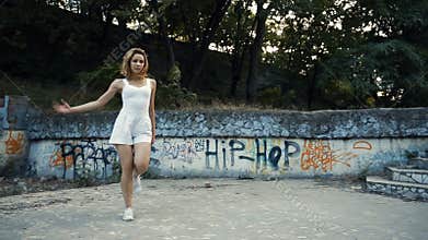 Woman dancing modern choreography in city park, outside. City ruins and graffiti.