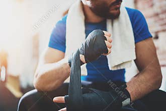 Muscular young boxer with black boxing bandages. Fists of fighter before the fight or training in sport gym. Blurred