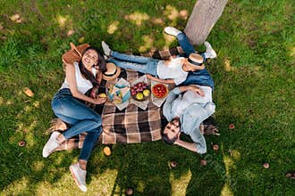 Multiethnic family eating and drinking while resting on plaid at picnic