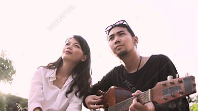 Asian younger man and woman relaxing emotion playing guitar outdoor