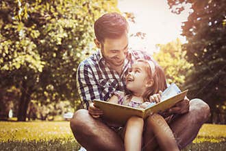 Single father sitting on grass with little daughter.