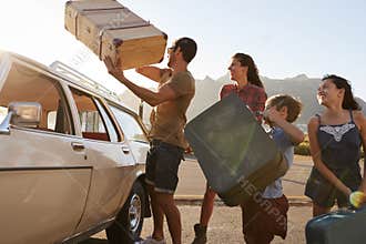 Family Loading Luggage Onto Car Roof Rack Ready For Road Trip