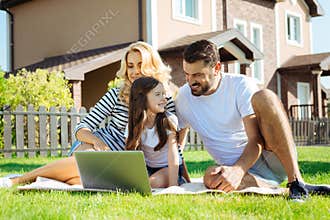 Happy parents watching cartoons with their daughter in yard