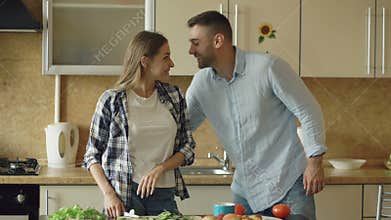 Happy young couple in the kitchen. Attractive woman cooking breakfast and cuff her boyfriend who want to taste food