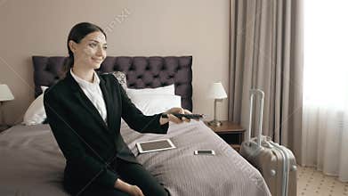 Young business woman relaxing in hotel room and looking tv, choose chanel with remote control