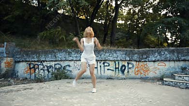 Young Asian woman dancing modern choreography in city park, outside. City ruins and graffiti Variety