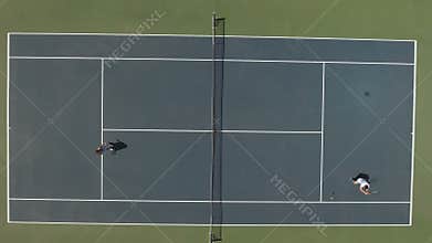 Cute woman in dress and young guy in shorts play tennis at the court