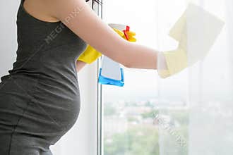 Young pregnant woman is cleaning window