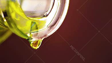 Pouring olive oil with macro drops by bottle on brown wood background