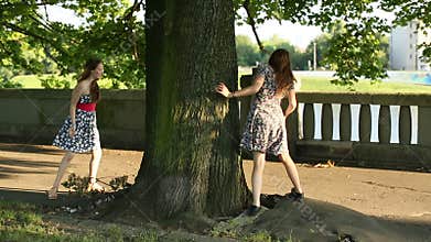 Two young teen girls play indulge in the Park, run around the tree.