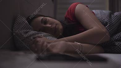 Young woman is sleeping in a cosy bed and then awakes and starts to use her mobile device.