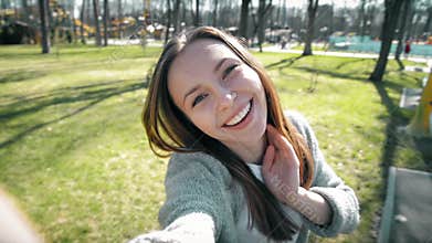 Portrait of a beautiful young woman selfie in the park with a smart phone.