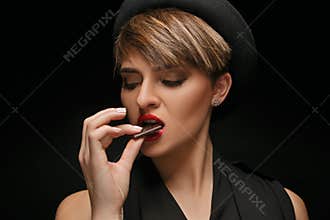 Attractive woman wearing black hat and classical t-shirt eat chocolate in a dark background.