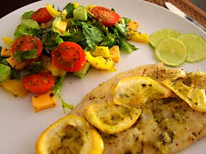 Fish baked in the oven with lemon and vegetable salad .