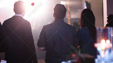 People standing back to camera and watching on a stage; musicians from the band playing music at corporate party.