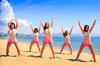 Cheerleaders dance on beach with hands upwards against azure sea
