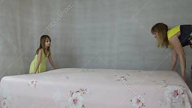 Mother with daughter make the bed bed sheets