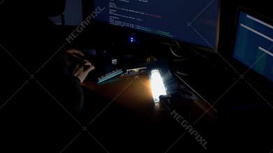 Hacker in hood cracking code using computers in dark room