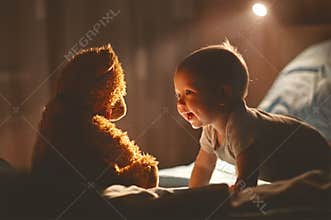 Happy baby laughing with teddy bear in bed