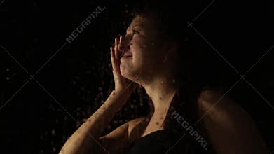 Young sad woman behind the window with drops on it. lonely girl drinking brandy from the bottle and crying