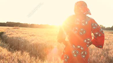 African woman in traditional clothes standing in a field of crops at sunset or sunrise