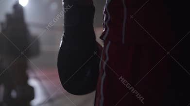 Close-up hand of unrecognizable sportsman in boxing gloves walking to ring in backlight. Confident calm Caucasian boxer