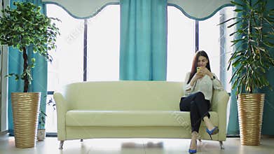 A general slow motion shot of a young dark haired career woman in a white shirt sitting on a sofa and chatting with her