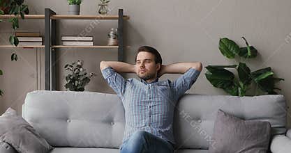 Man resting on couch put hands behind head feels serene