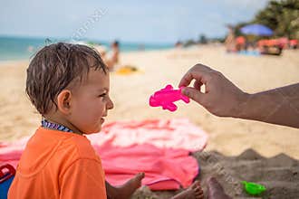 End quarantine concept, restrictions lifted, borders open. A little cute toddler sits on the beach, looks at a toy